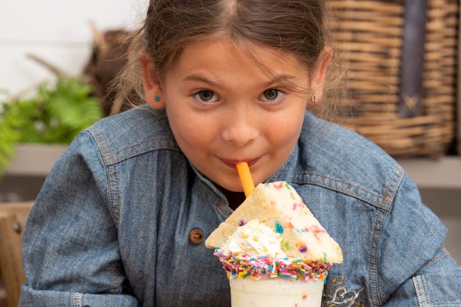 little girl drinks milkshake with slice of cake on top